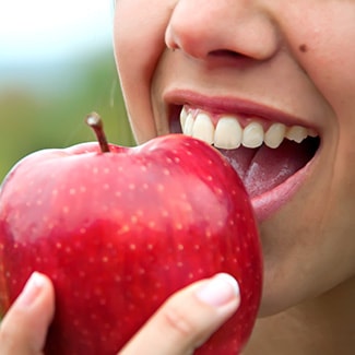 A lady biting into an apple, thanks to Invisalign